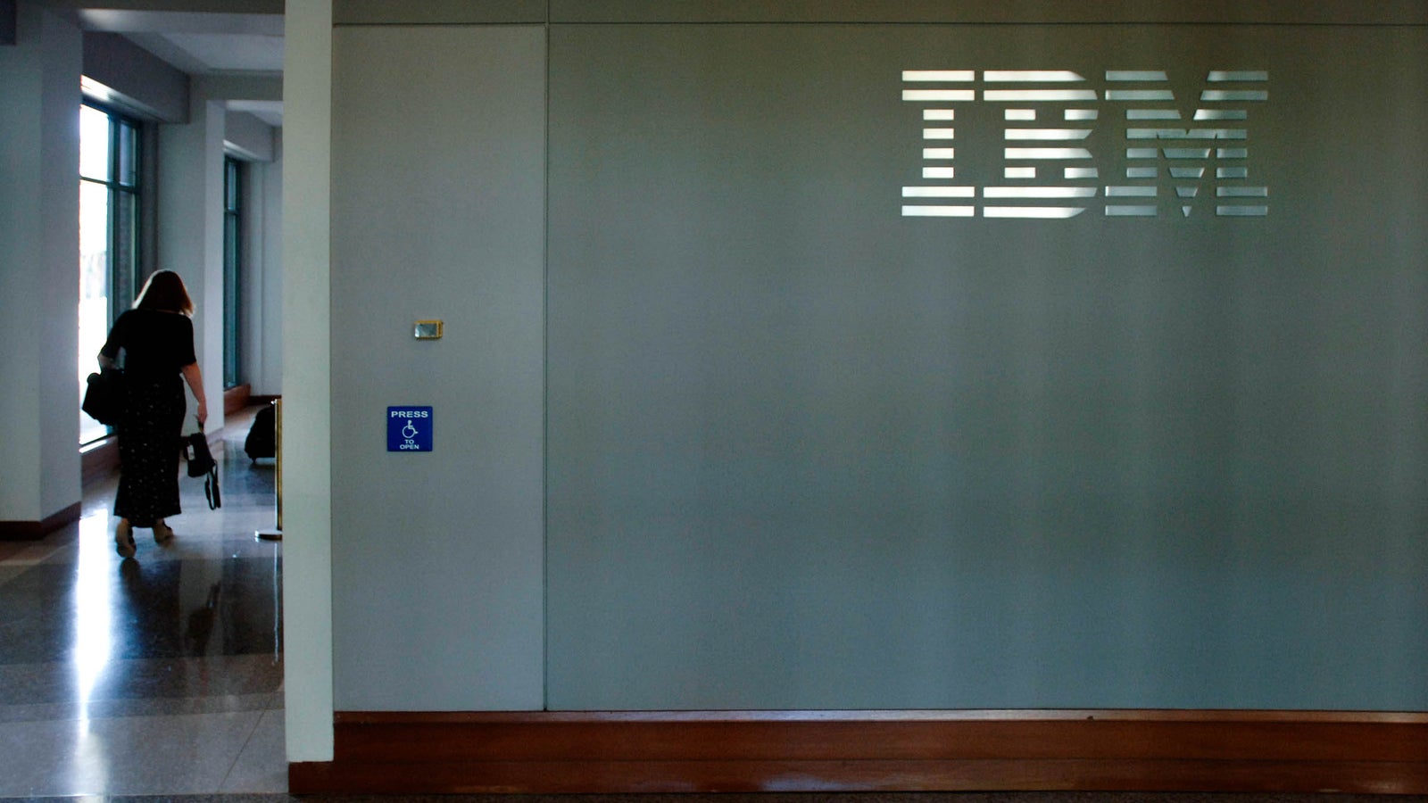 A person walking out of an IBM office, the IBM logo is visible on the wall.