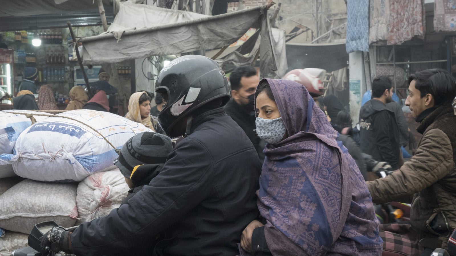 A closeup of people wearing face masks riding a bike near a street market in Lahore.
