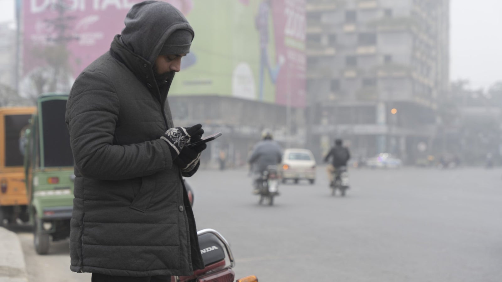 Delivery rider Sami Iqbal checks his phone by the side of street covered in smog.