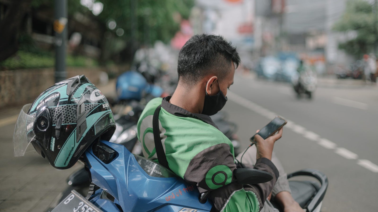 A Gojek delivery rider resting on his bike using a phone.