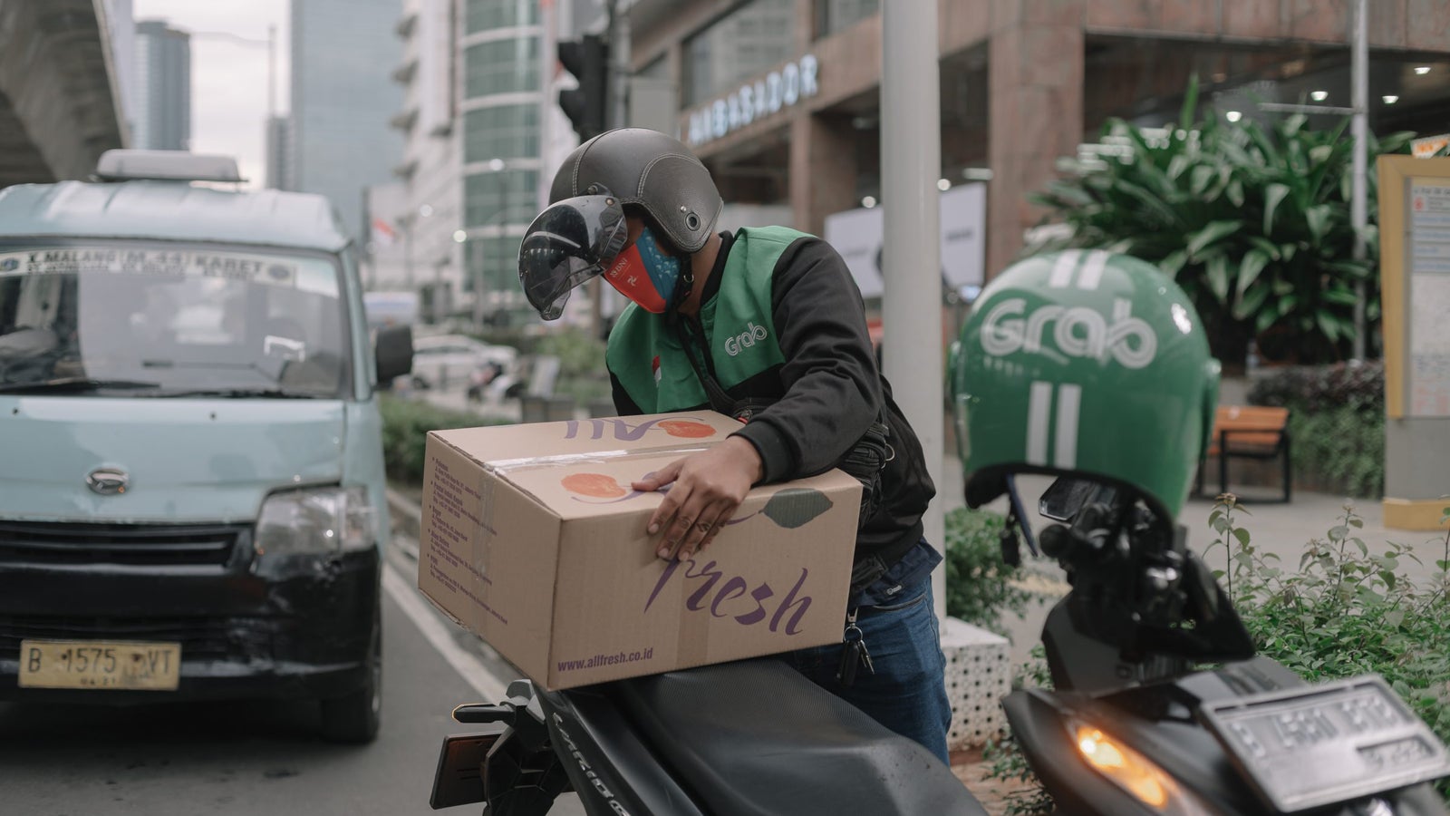 A photo of a delivery worker holding a package on the seat of his motorcycle