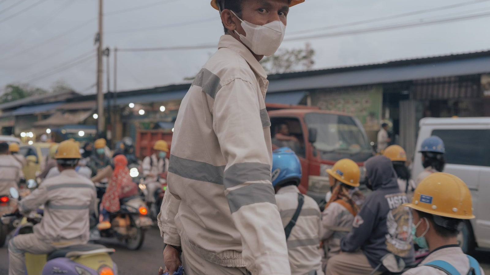 A portrait of a nickel miner wearing his uniform and helmet, surrounded by motorists.