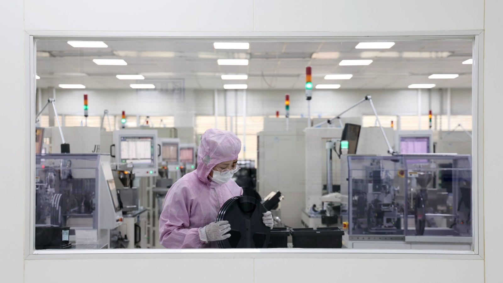 A photo showing a worker in a semiconductor factory behind a glass frame.