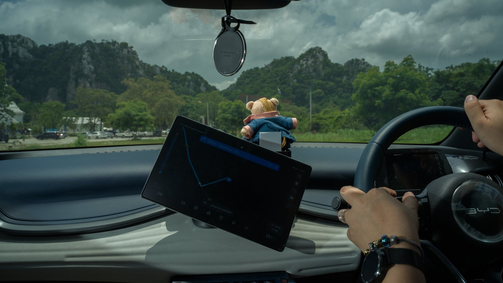 Inside of a BYD car overlooking mountains, a drivers' hands on the steering wheel.