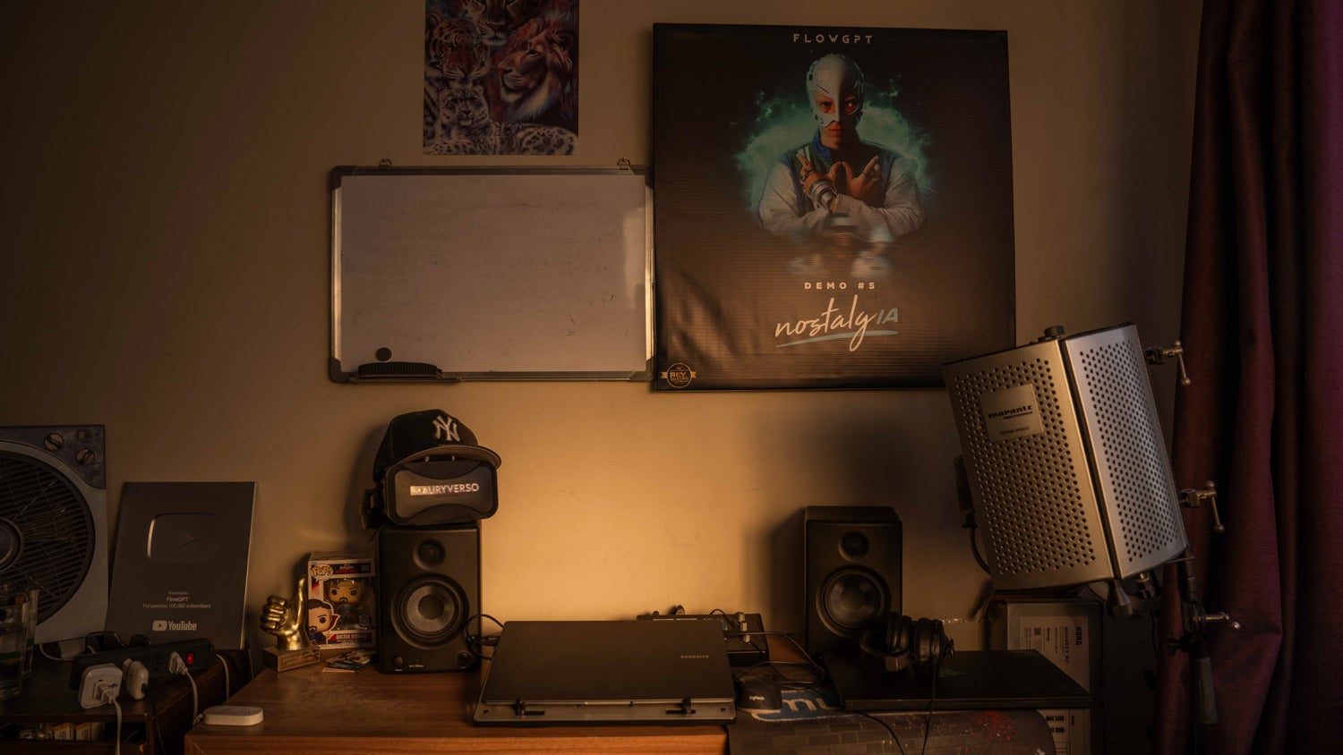 Mauricio Bustos' computer is on a small desk in his room, along with speakers his cap and other items. On the wall is a whiteboard and FlowGPT poster.