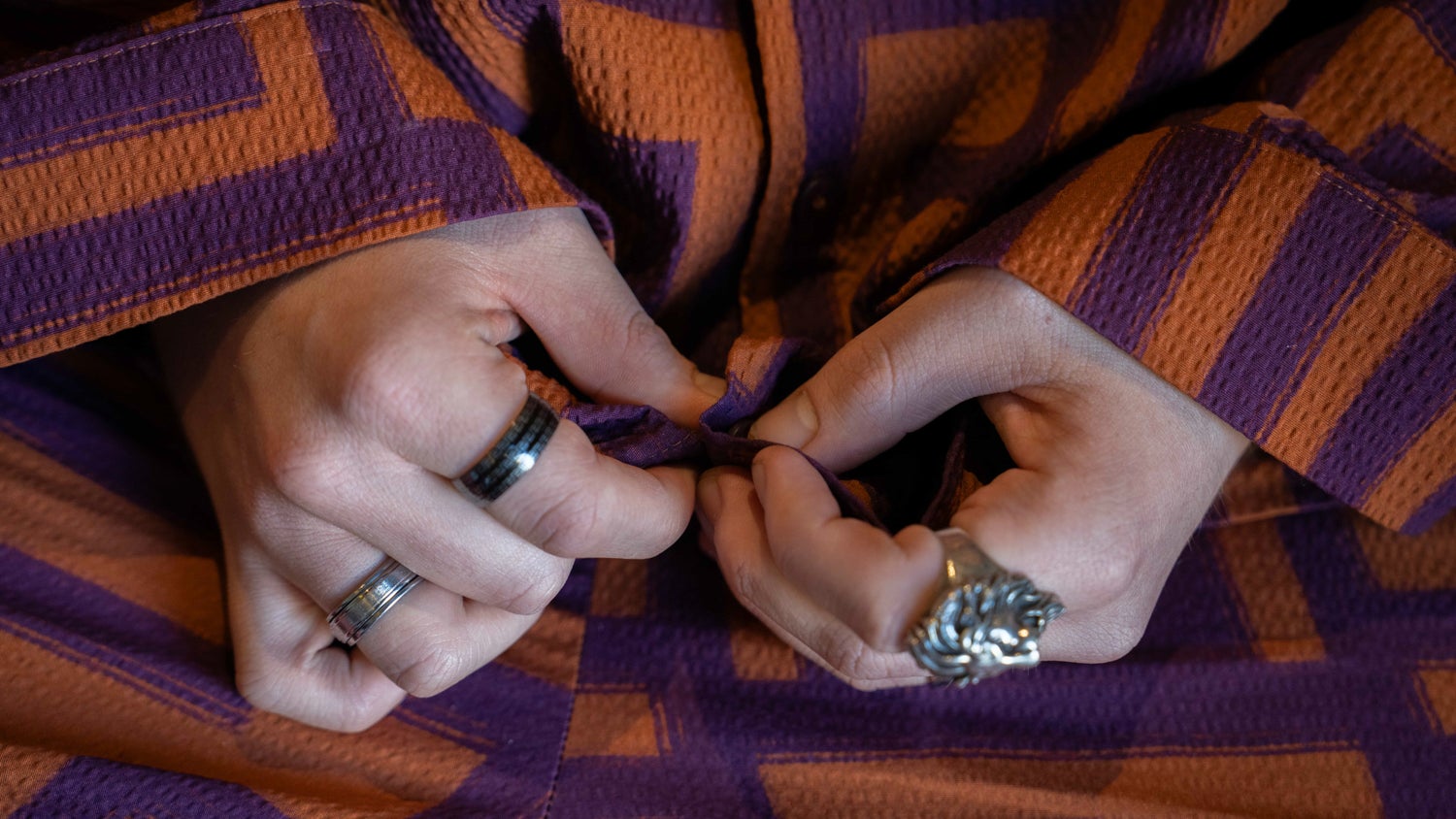 A closeup of hands wearing multiple rings. The person is wearing a bright purple and orange outfit.