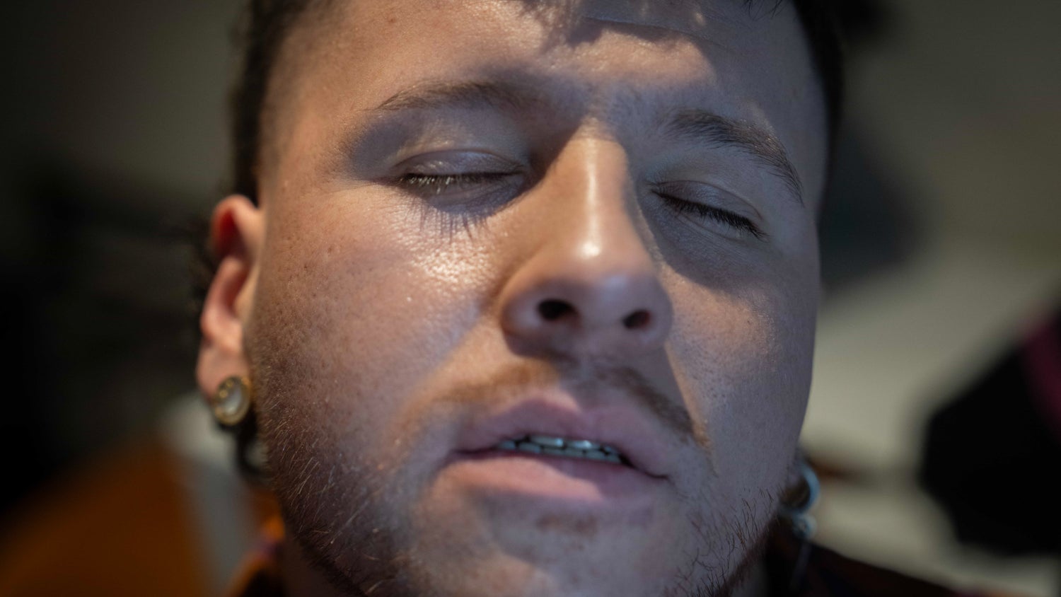 A closeup portrait of Mauricio Bustos, his eyes are closed and face titled upwards with his mouth slightly open, there is a slight shadow casted from above.