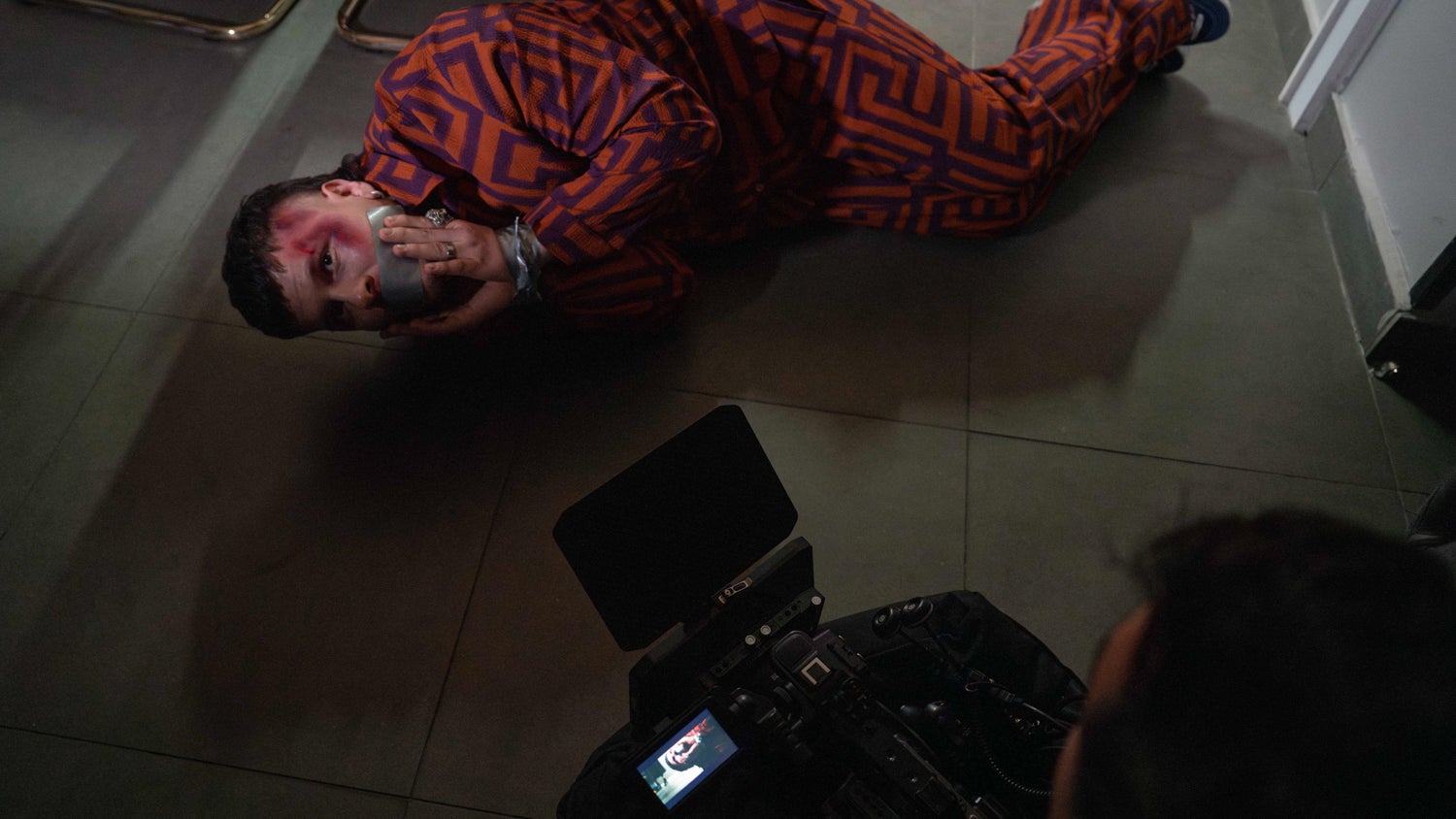 A photograph of Mauricio Bustos lying curled up on the floor facing a video camera with his hands and mouth taped, with a bruise on his forehead.