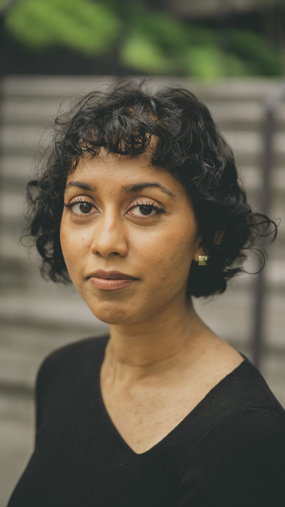 A close photograph of a woman wearing a black shirt, with short hair, against a blurred background of steps.