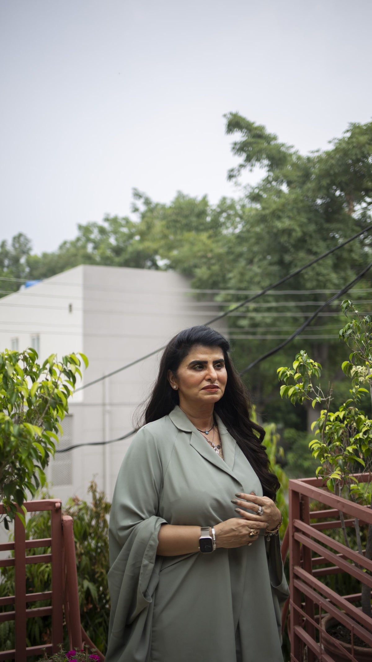 A portrait photograph of a woman wearing a green shall and standing outside near greenery.