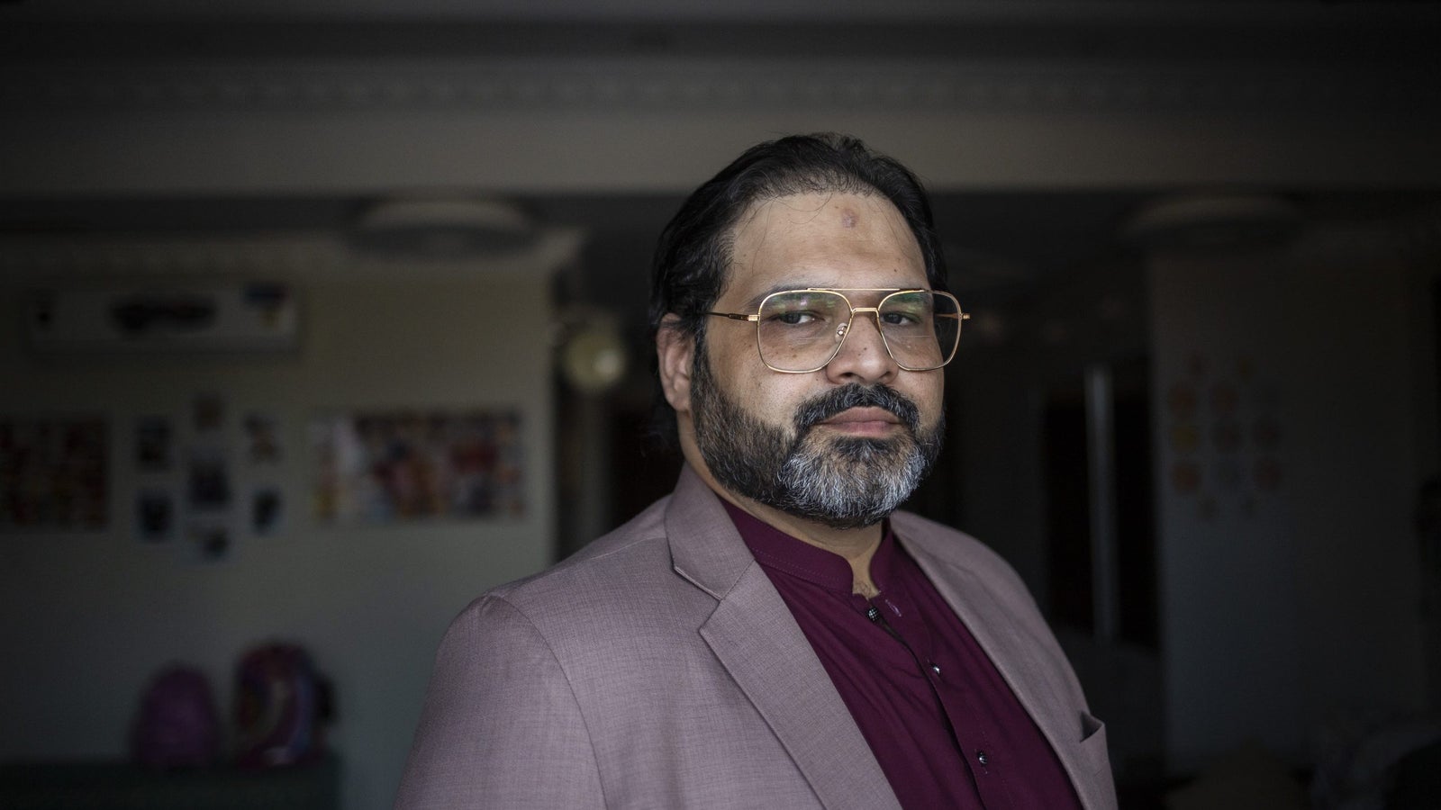A portrait photograph of a man with glasses and a beard, wearing a maroon jacket and dress shirt.