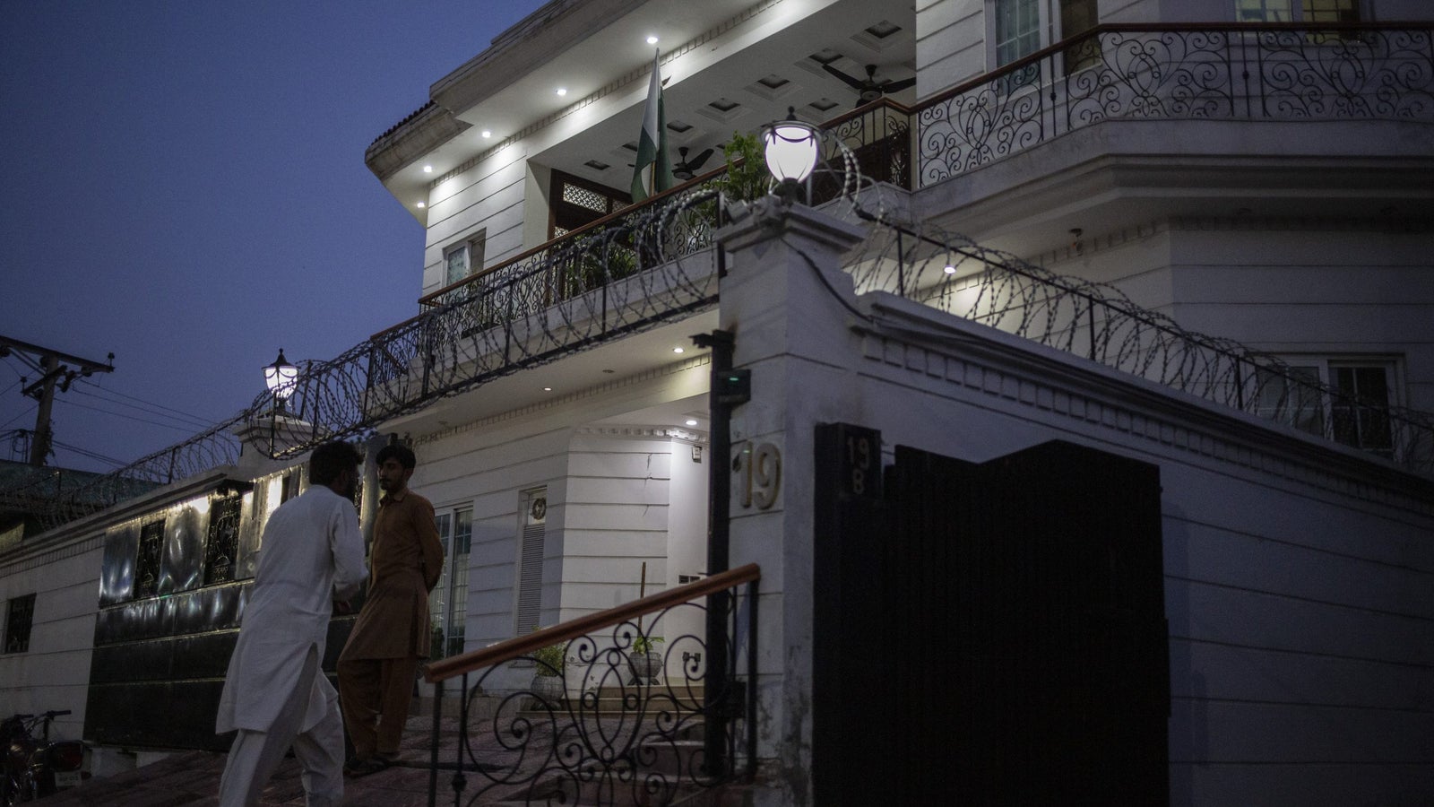 A photograph showing the exterior of a white compound, ringed with barbed wire, at night.