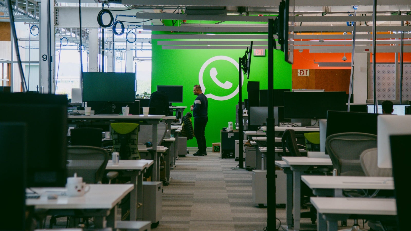 Interior of WhatsApp headquarters at Meta’s MPK 21 corporate campus in Menlo Park. A person is seen standing between rows of desks, and various computer monitors are visible throughout the space.
