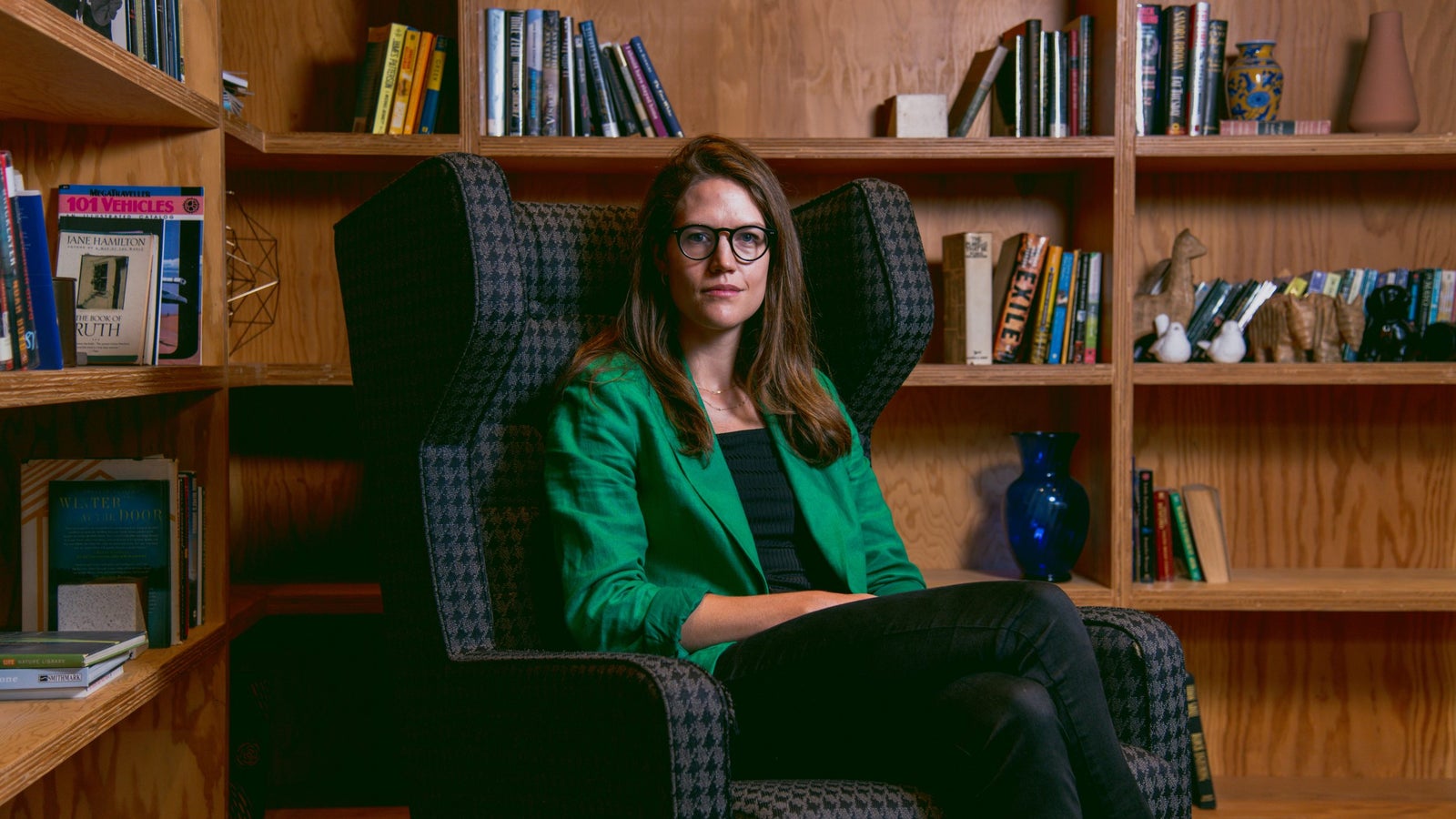 A portrait of Alice Newton-Rex, vice president of product at WhatsApp, at Meta’s corporate campus, wearing a green blazer seated infront of a wooden bookshelf.