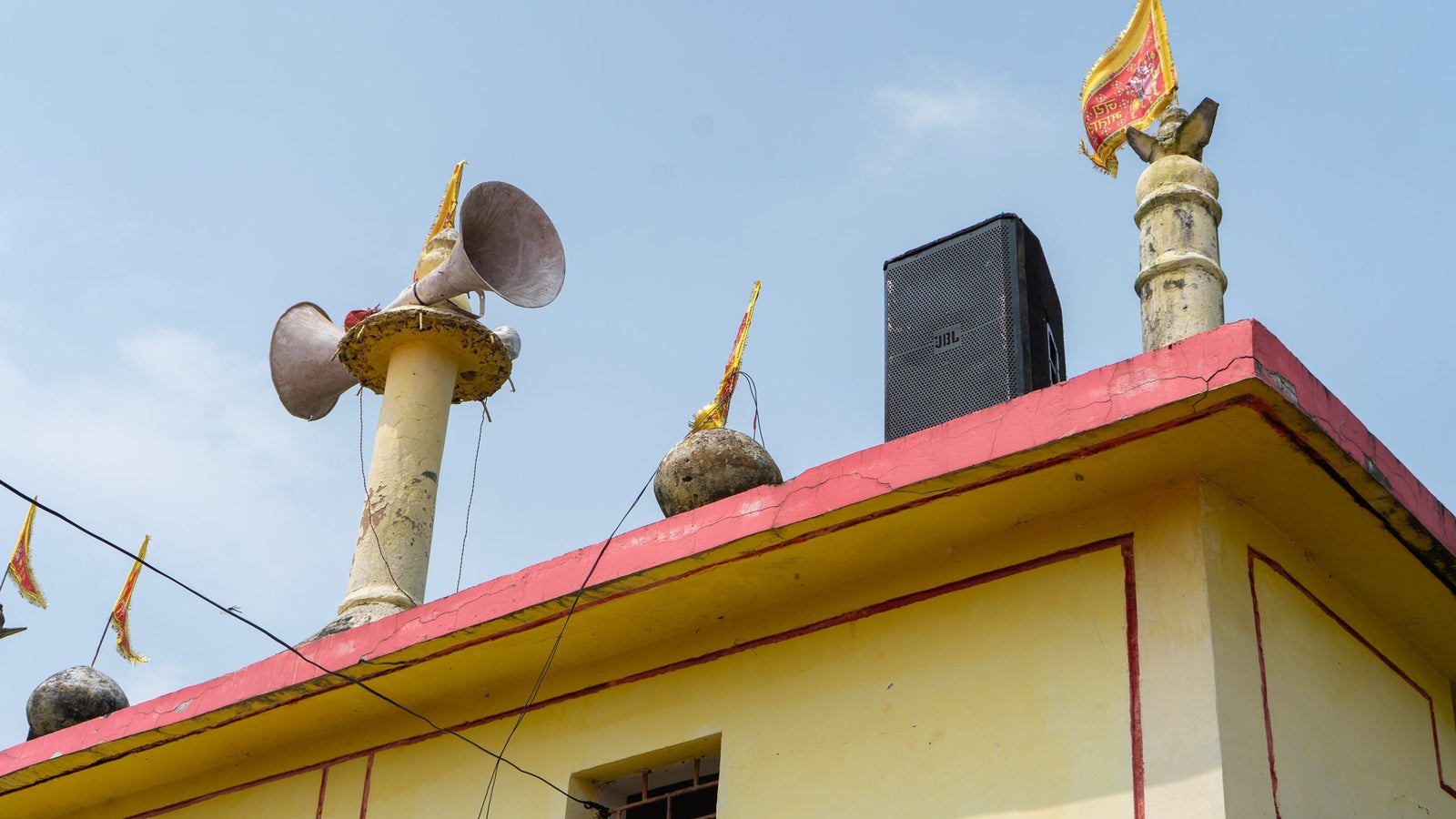 Loudspeakers and a JBL speaker on the corner of a building roof.
