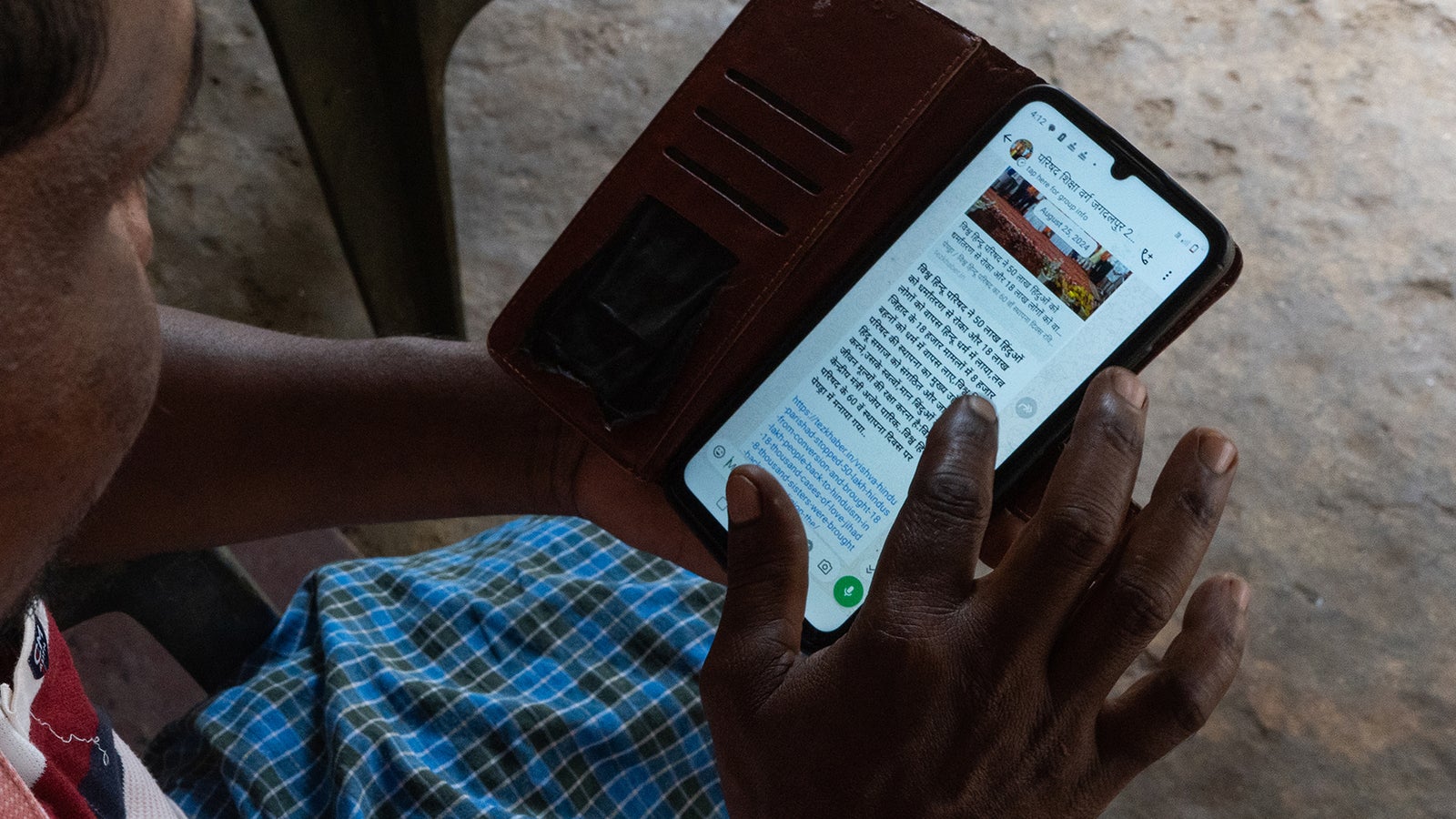 A photo of a person using a phone, on the screen is a whatsapp chat in Hindi.