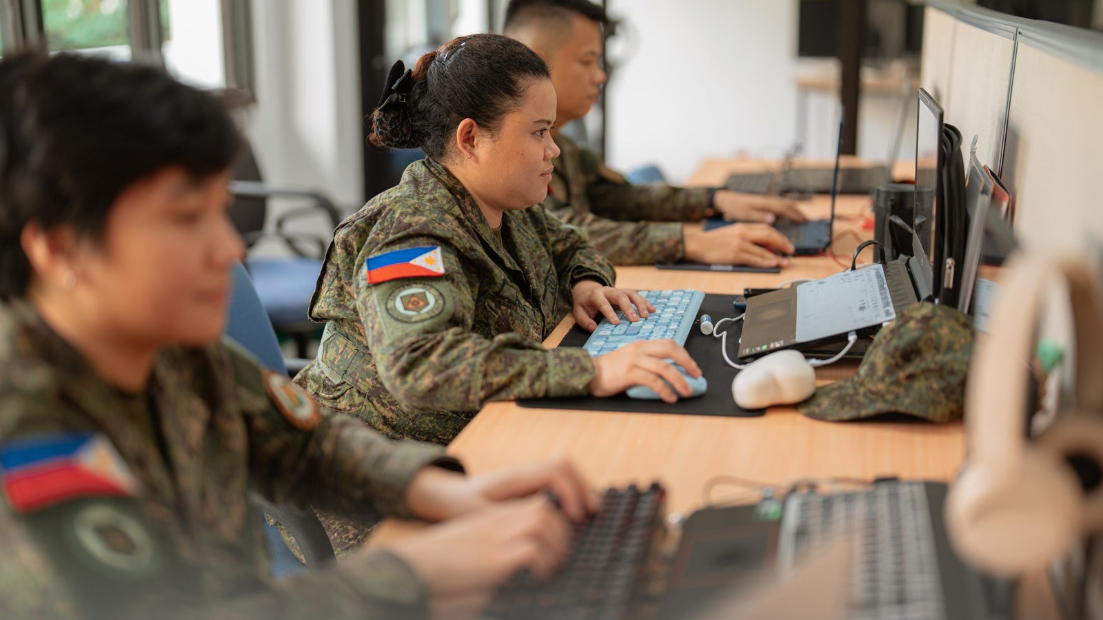 A group of Philippine's Cybersecurity Battalion in camouflage uniforms working at computers in an office setting.