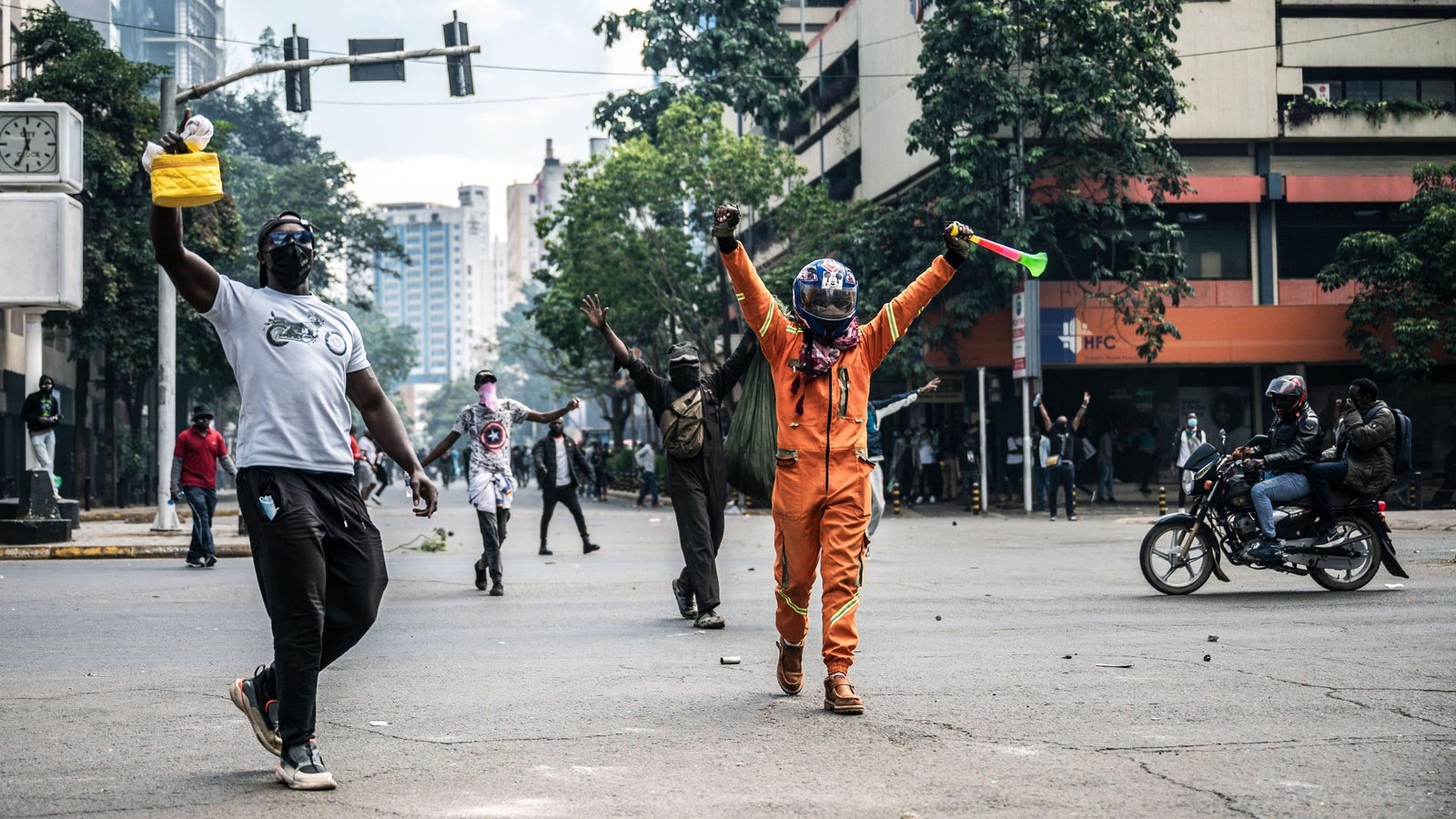 A photo showing men scattered at a road intersection with their hands raised in their air, their faces covered with helmets and scarves.