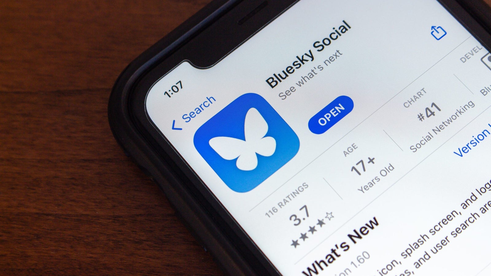 A smartphone displaying the app page for "Bluesky Social," featuring a blue icon with a white butterfly. The background is a wooden surface.
