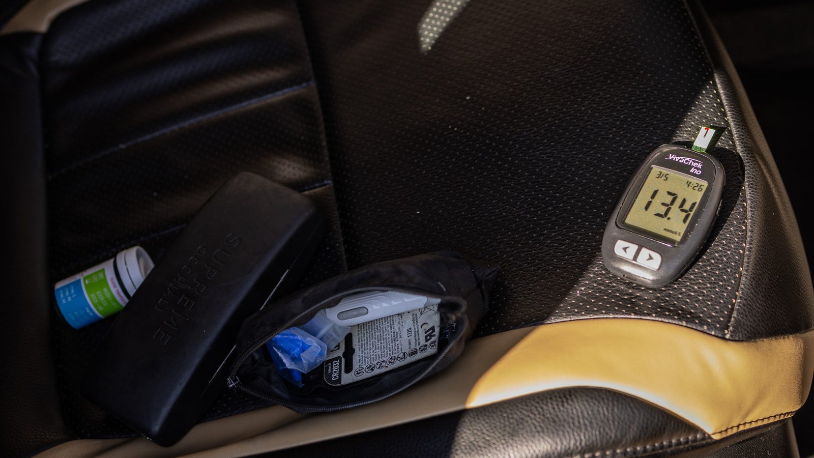 A car seat with medical items on it, including a blood sugar reader, a pouch and a medicine box.
