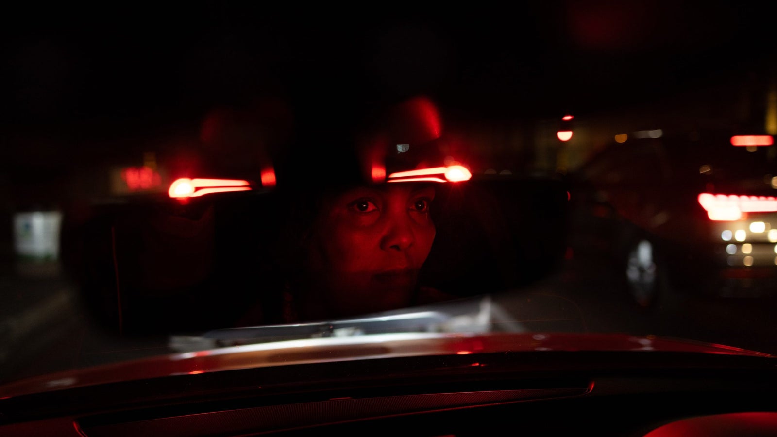 Nolwazi Mtshekexe at night, seen in the rearview mirror lit up by red lights.