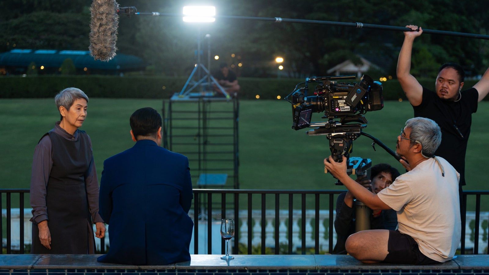 A photo showing a film production scene outdoors, with people holding video and audio equipment.