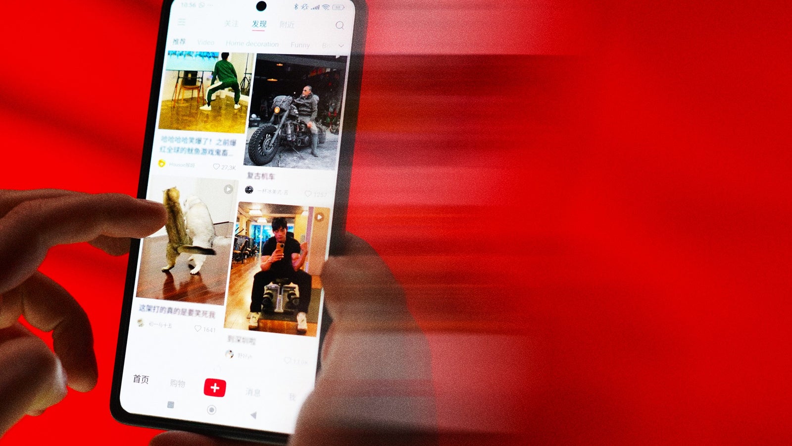 A close-up of a smartphone held by a person with two fingers, displaying the social media app Xiaohongshu interface filled with images and text. The background is a vibrant red, adding motion blur effects to the scene.