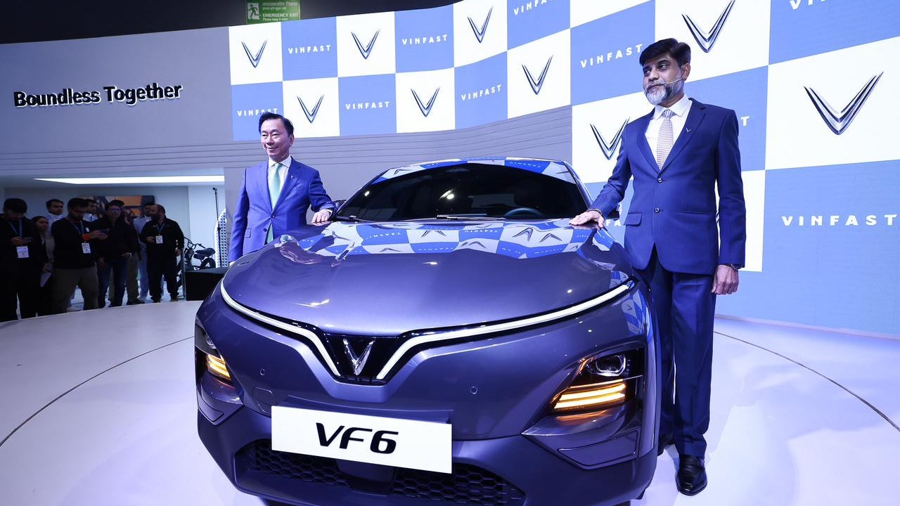 Two men in suits stand beside a new VinFast VF6 electric car on display at an exhibition, with a background featuring the VinFast logo and the phrase 'Boundless Together.'