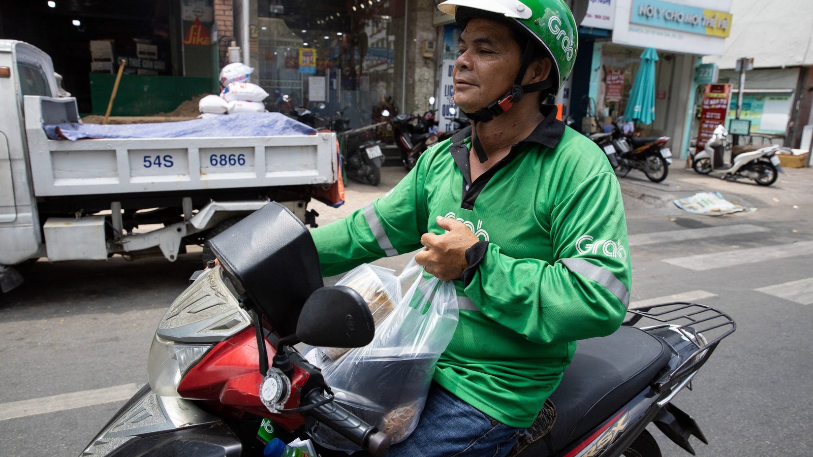 Nguyen Van Sau holds onto a food delivery parcel while driving his motorbike.
