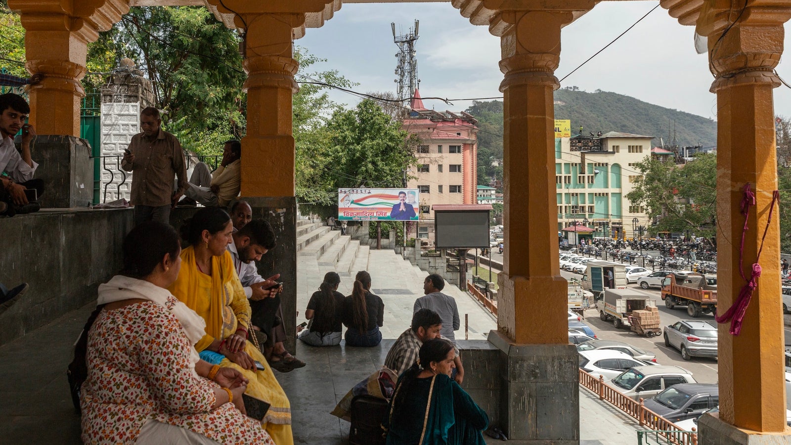 A photography showing a number of people seated on steps overlooking a downtown in India, with mountains in the background.