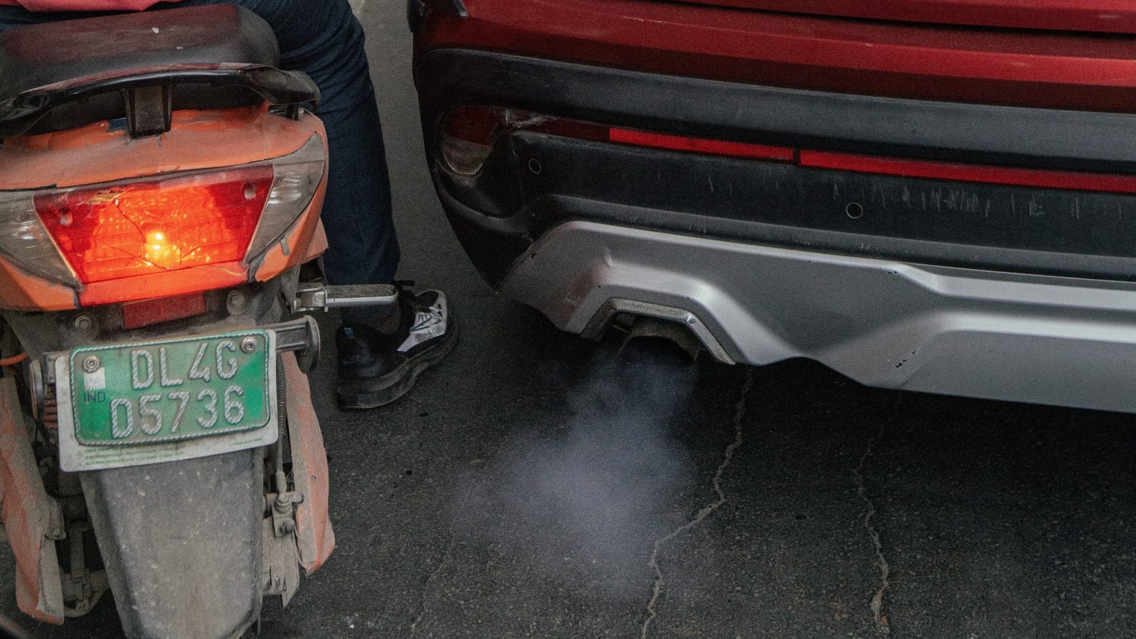 A closeup of a car exhaust with fumes next to a motorbike.