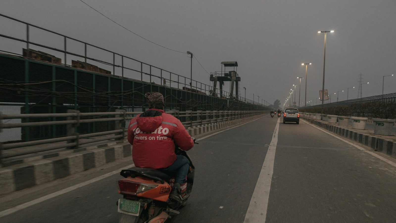 Zomato's delivery partner, Mannu Kumar, rides his bike across a bridge, with a hazy skyline ahead.
