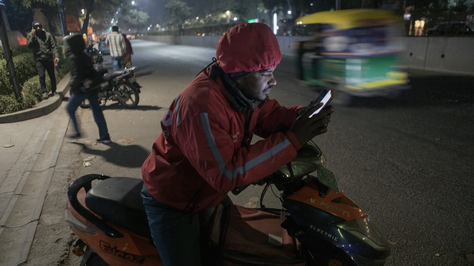 Zomato's delivery partner, Mannu Kumar, checks his phone while parked on his bike by a street.