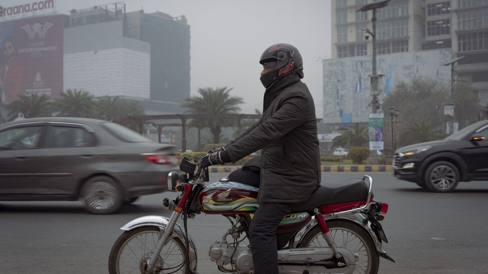 A photo of a man sitting on a motorbike on a busy street in Lahore, Pakistan.