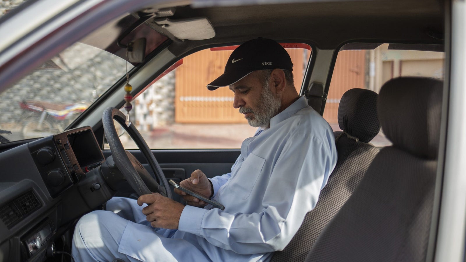 Basharat Buraak checks his phone while seated in the drivers seat of his car.