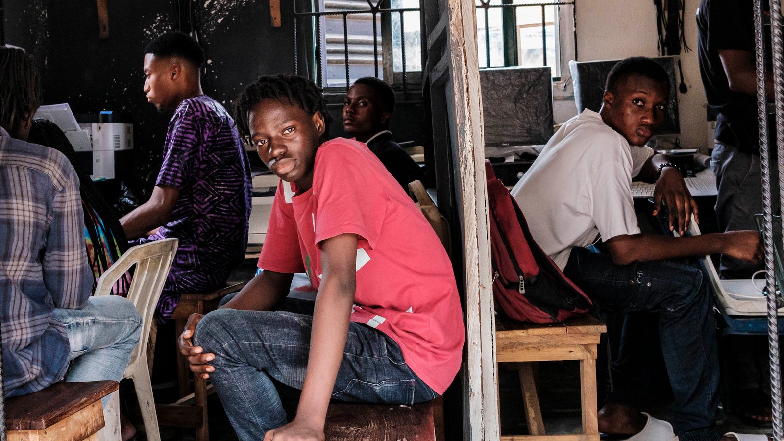 A photo of a group of young men, split into two rooms with computers in the background. Two of the young men are looking directly at the camera.
