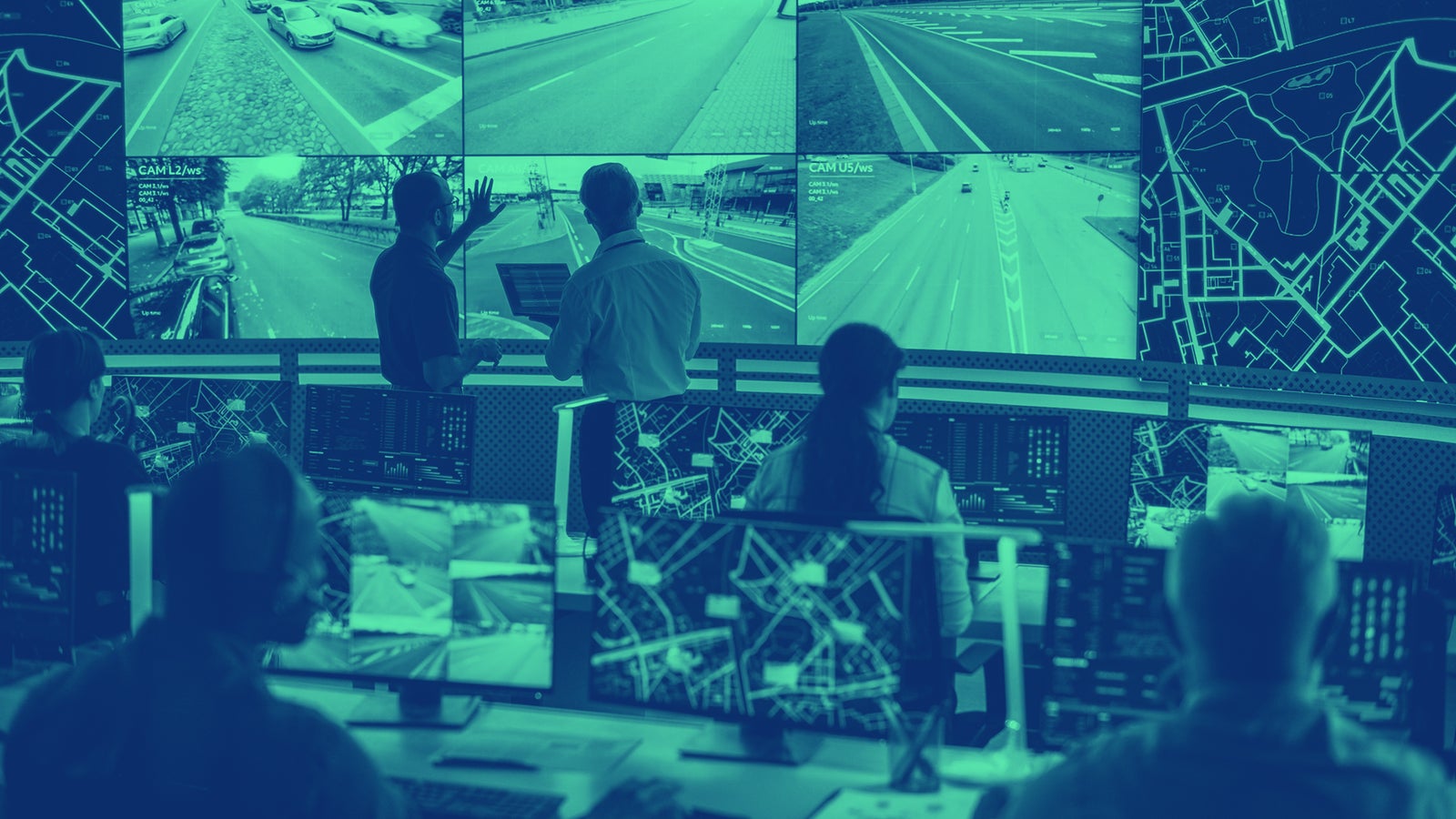 A control room with multiple monitors displaying live traffic footage and maps, where several people are engaged in a discussion about the data. The room is equipped with advanced technology for surveillance and monitoring.