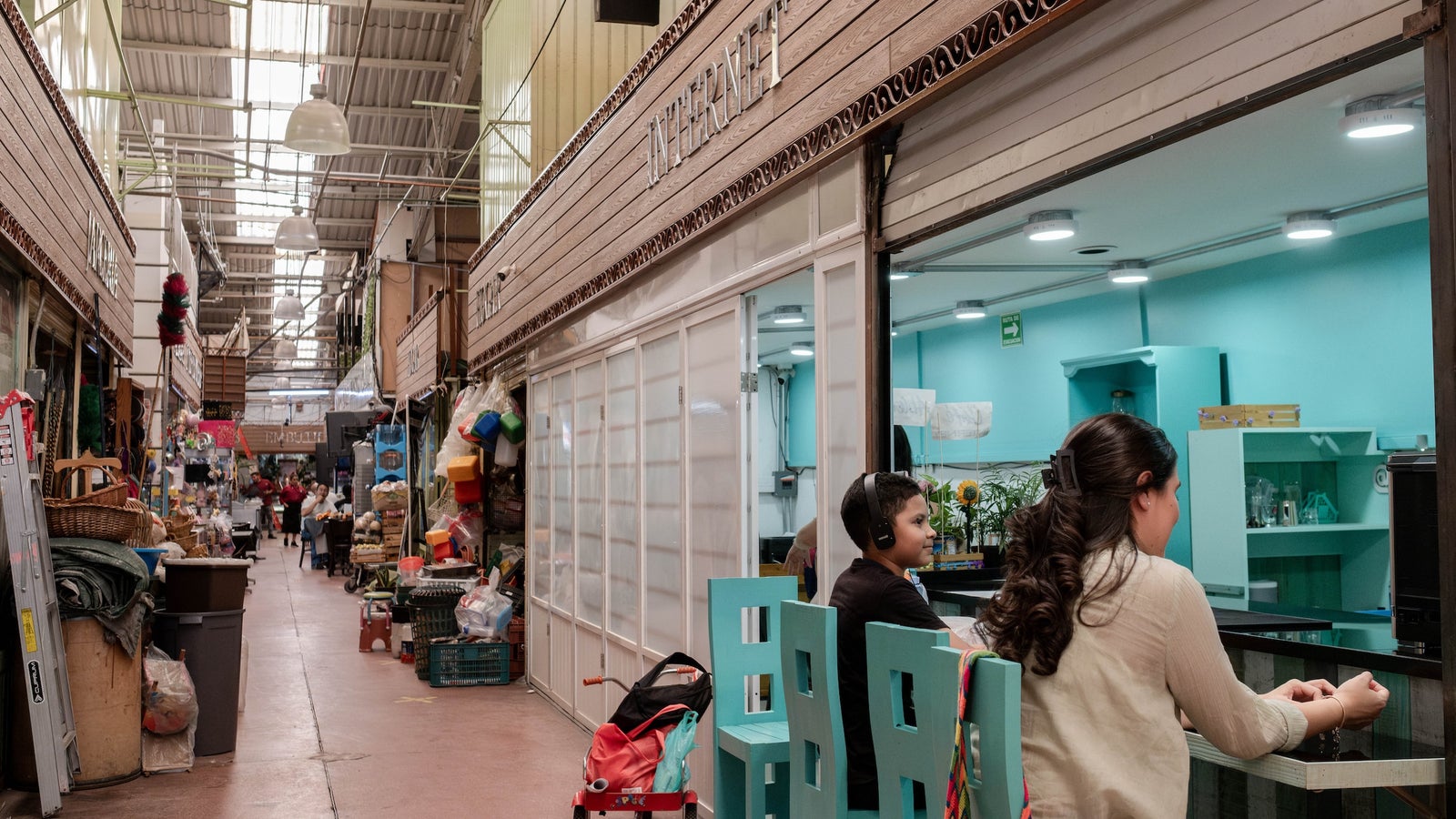 A photo of a woman and child sitting on a teal chairs inside a marketplace.