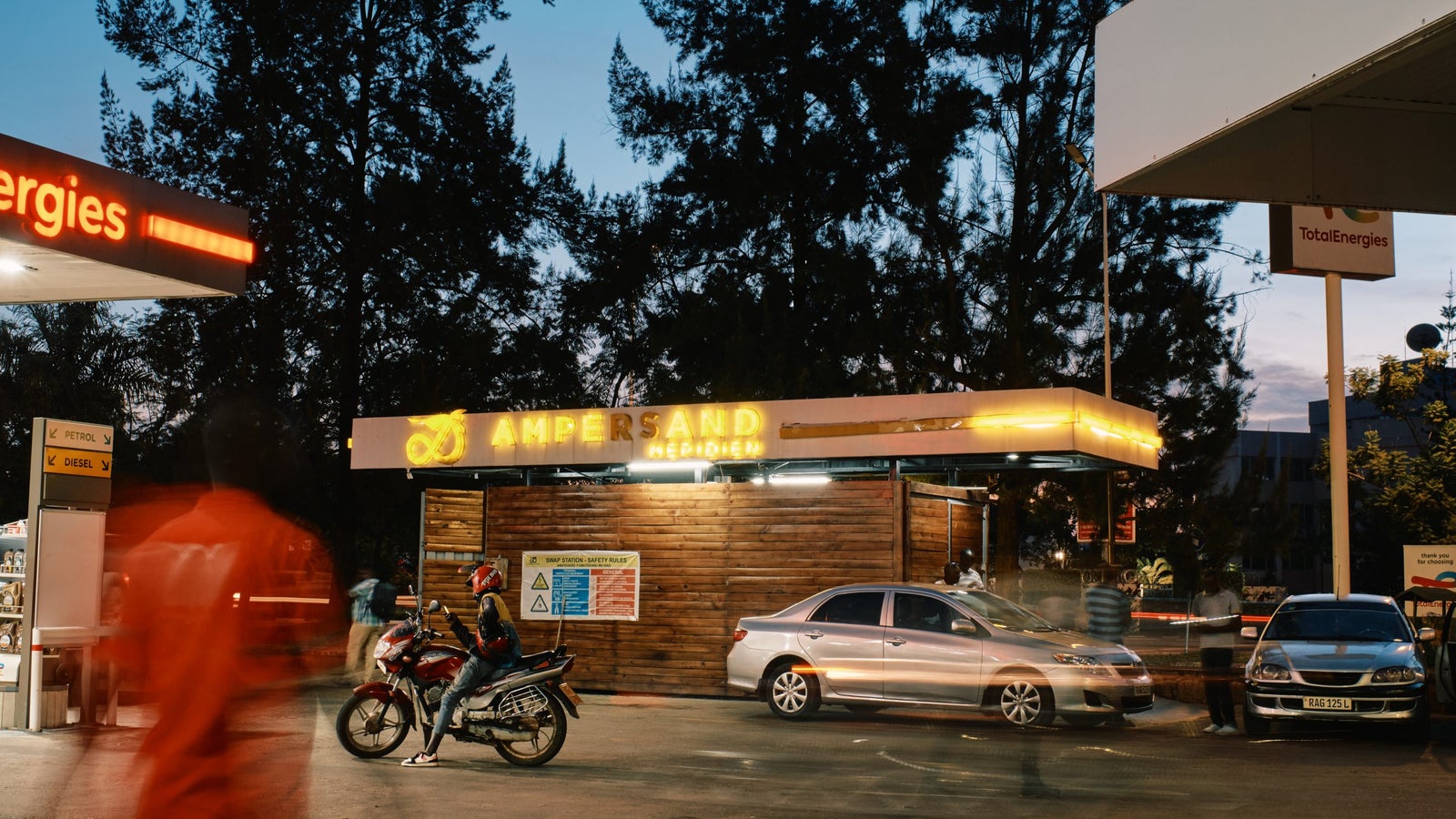An Ampersand battery swap station in the evening with a slow shutter blur of people walking around.