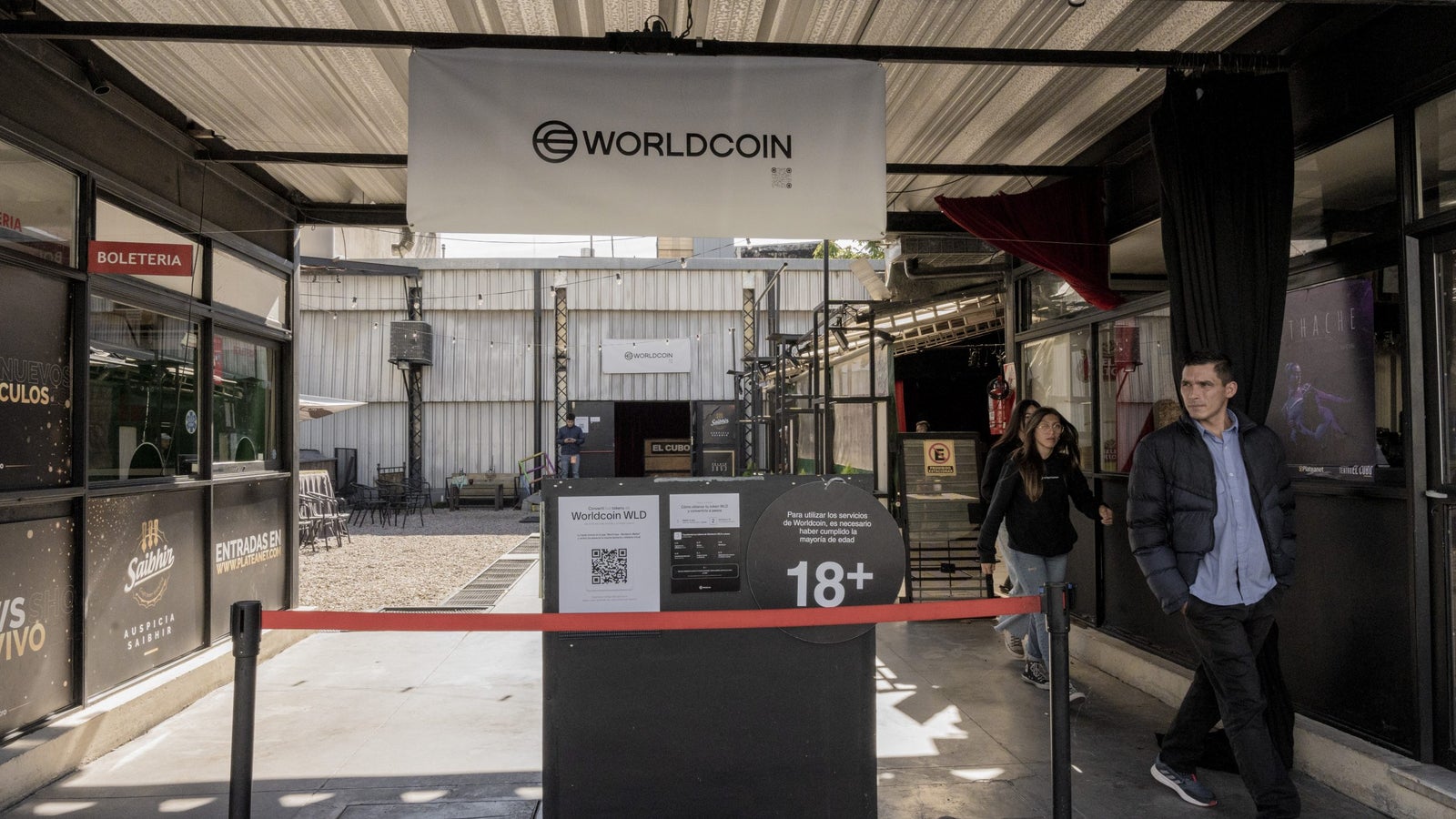 A Worldcoin banner hangs over a club entrance with people walking out besides it.