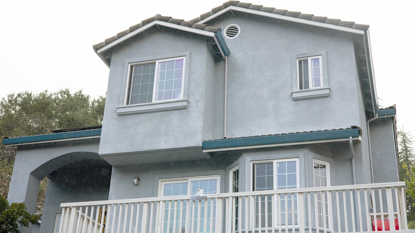 A two-story gray house with a balcony, featuring large windows and a tiled roof.