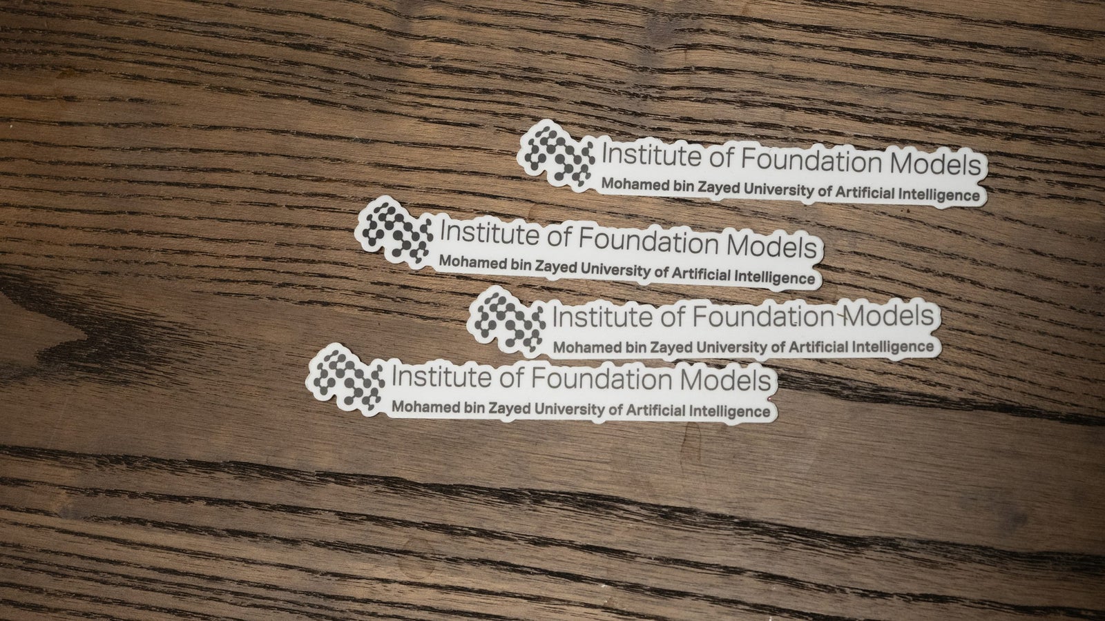 Three stickers displaying "Institute of Foundation Models" and "Mohamed bin Zayed University of Artificial Intelligence" on a wooden table.