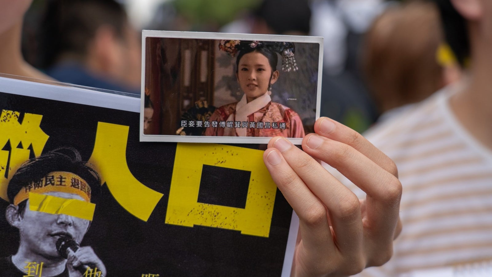 A photography of a hand holding up a sign and a meme, showing subtitled text on a photo of a woman in traditional Taiwanese clothing.