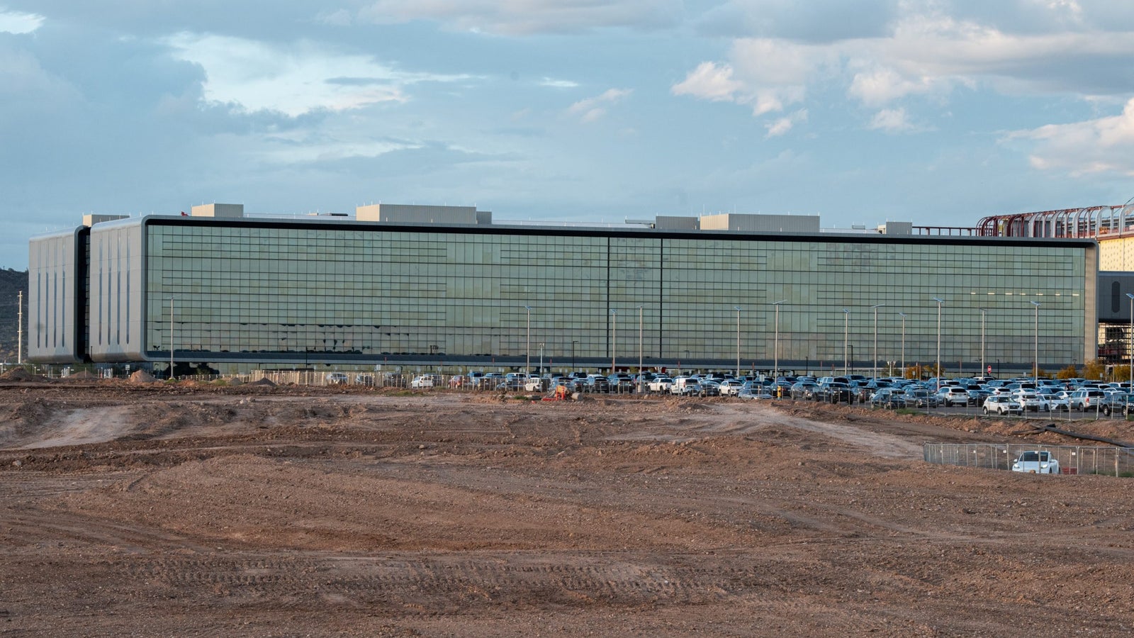 A photograph of a large glass building behind of barren dirt field.