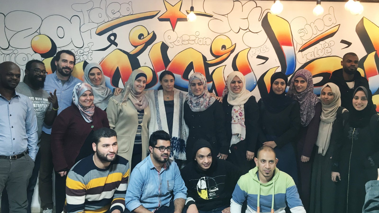 A diverse group of people posing for a photo in front of a colorful graffiti mural in a social setting.