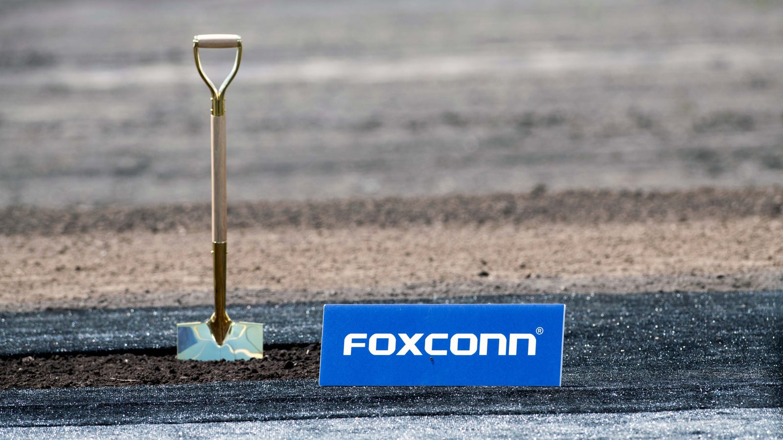 A photo of a shovel set in the ground besides a Foxconn logo.