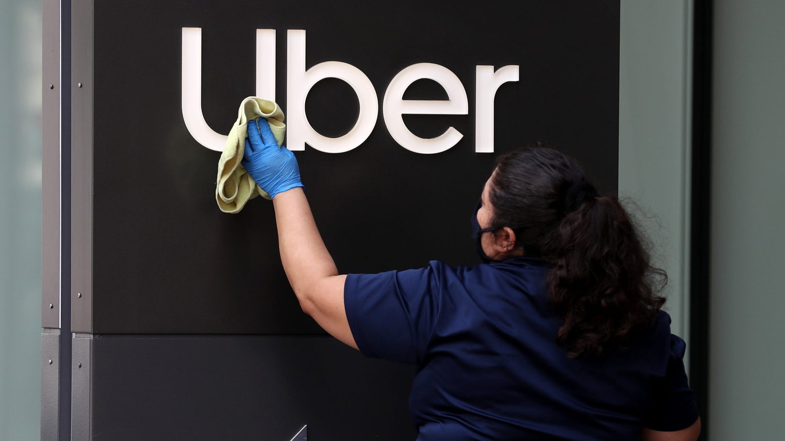 A worker cleans a sign in front of the Uber headquarters