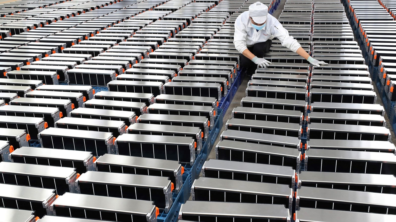A photo showing a person between rows and rows of large, silver car batteries.