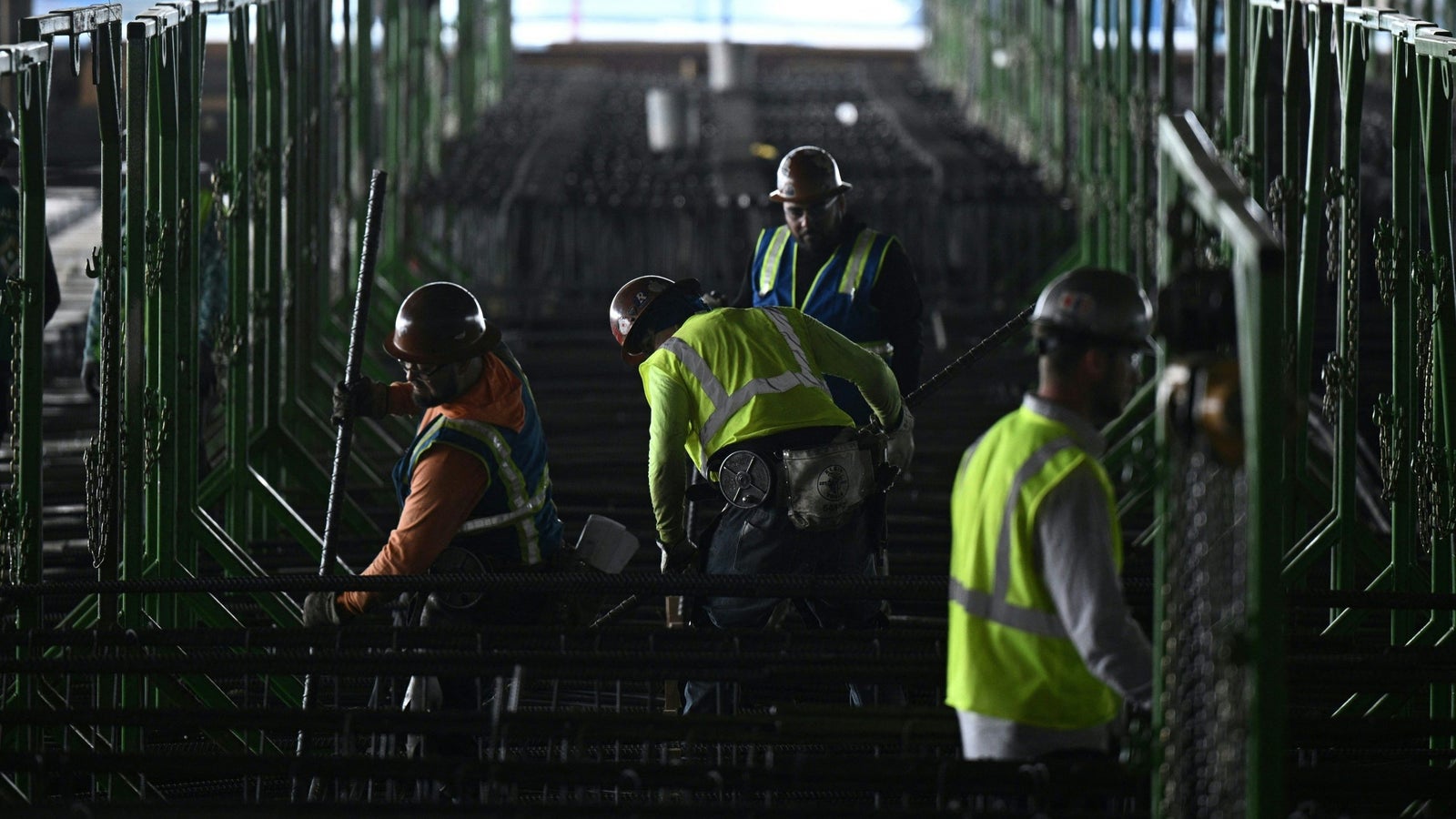 A photograph of construction workers moving metal equipment in a dark environment.