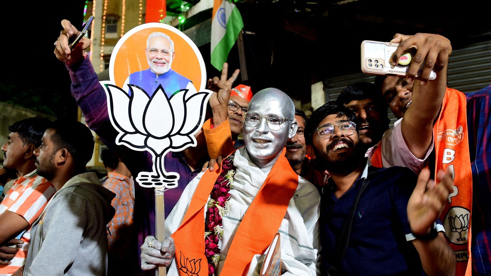 A photo of Bharatiya Janata party supporters taking selfies with a person painted in silver.